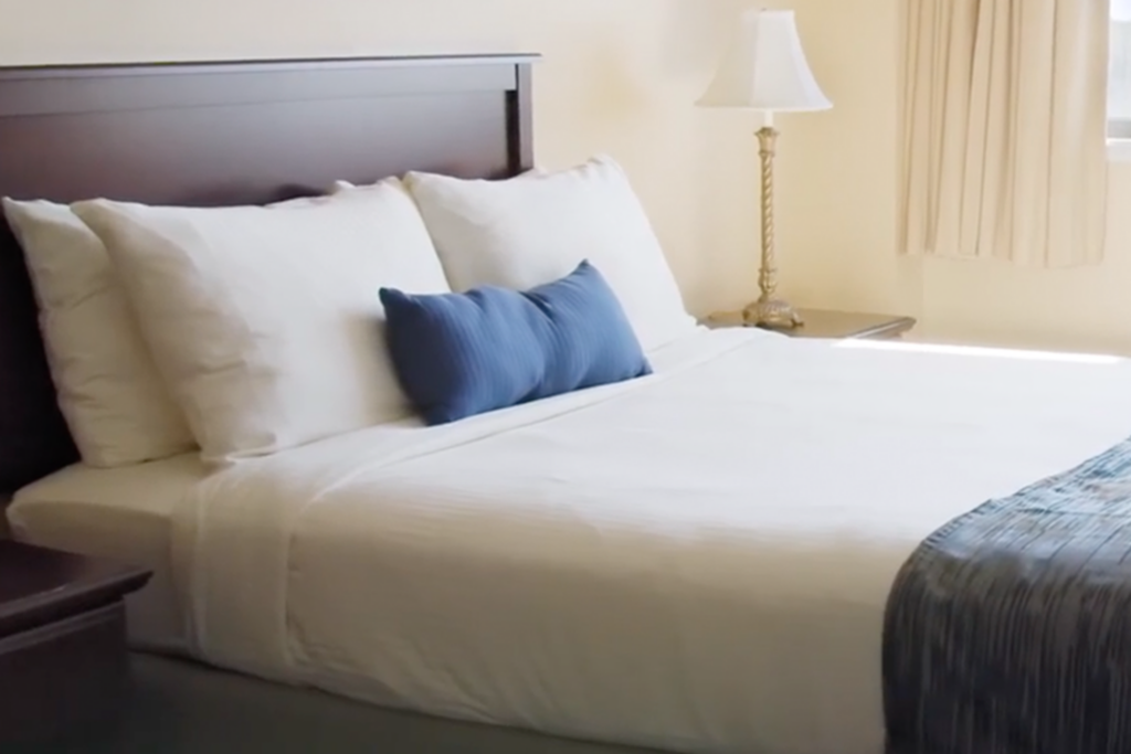 a hotel bed with white sheets and a blue pillow