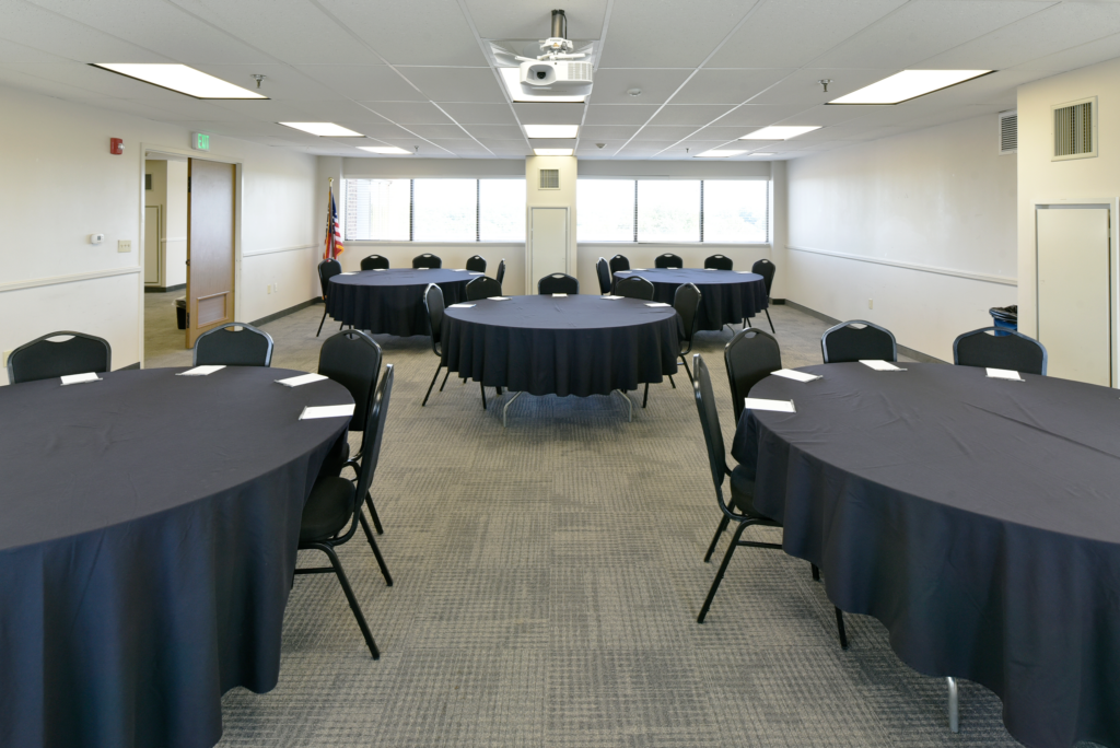a conference room with circular tables, chairs, and a projector screen